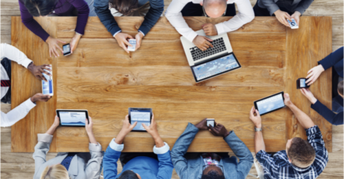 Working professionals sitting around desk using technological devices. 